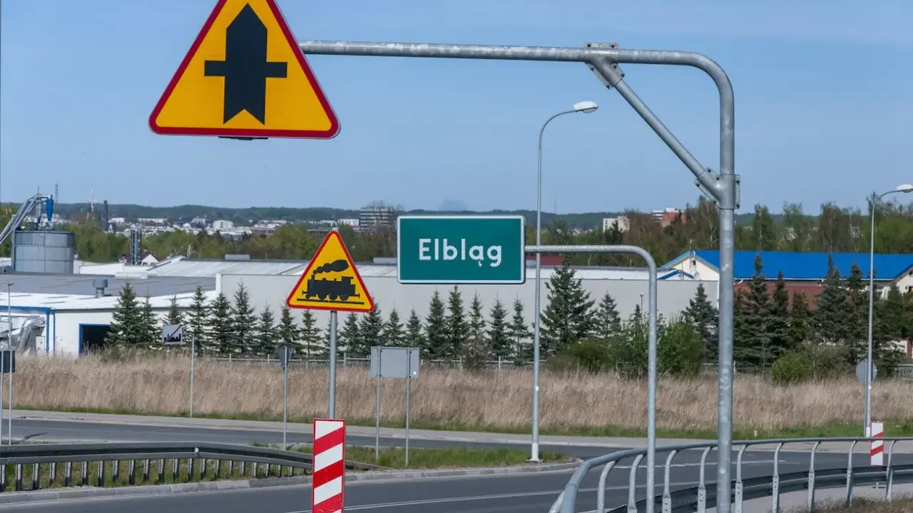 Uwaga na skrzyżowanie z drogą podporządkowaną i przejazd kolejowy. Znak "Elbląg" zaprasza do miasta.