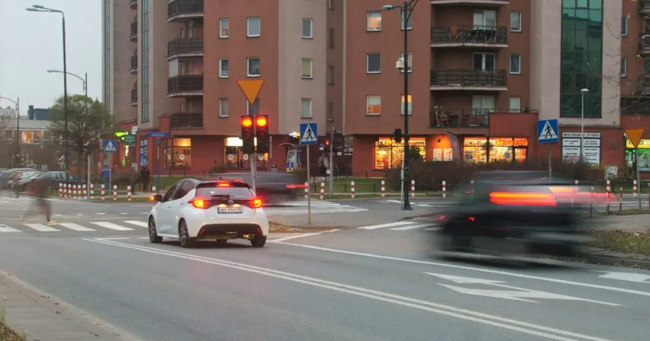 Biały samochód czeka na zielone światło. Czerwone światło oznacza punkty karne.