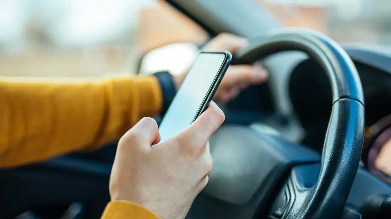 Ręka trzymająca telefon za kierownicą. Zastanawiasz się, ile punktów za telefon stracisz?