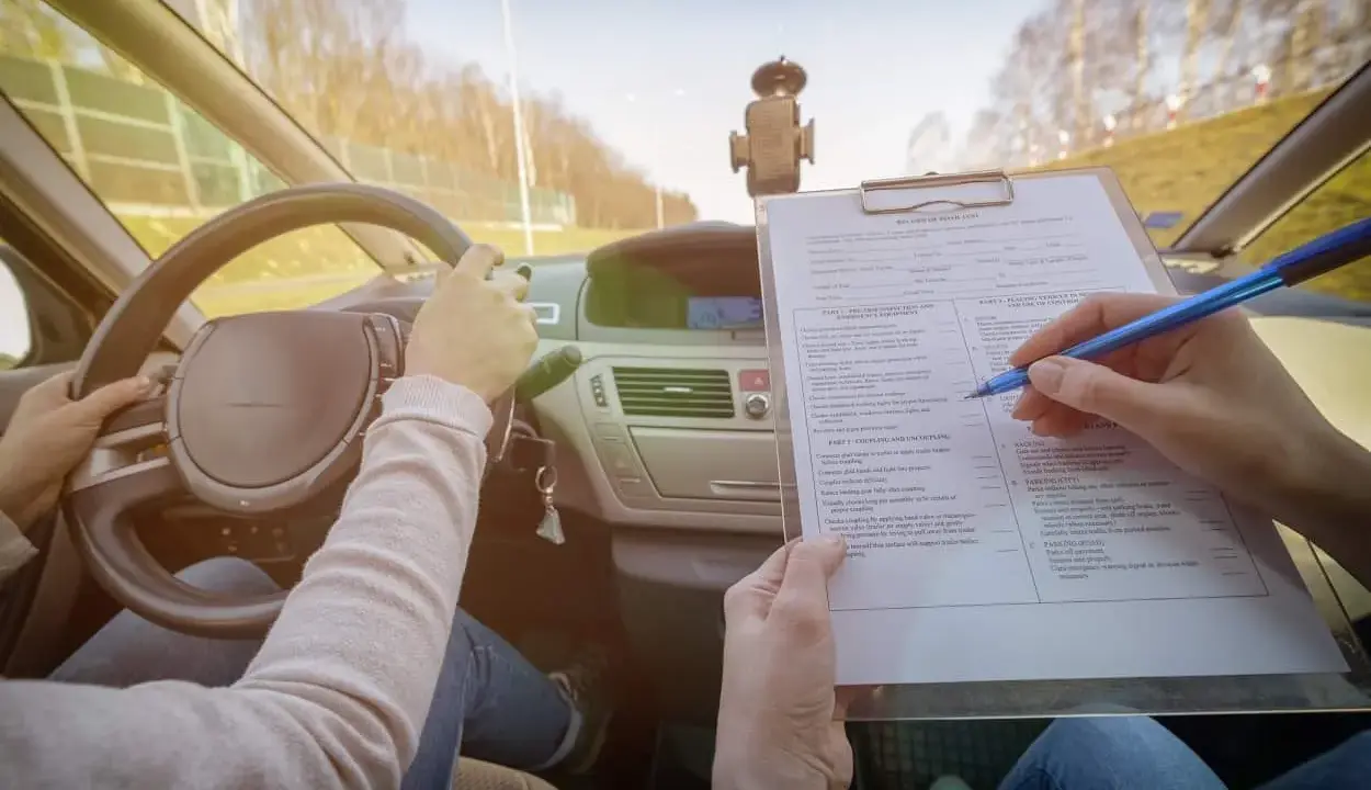 Egzamin na prawo jazdy. Kandydat trzyma kierownicę, a egzaminator wypełnia formularz oceny, sprawdzając kategorie prawa jazdy.