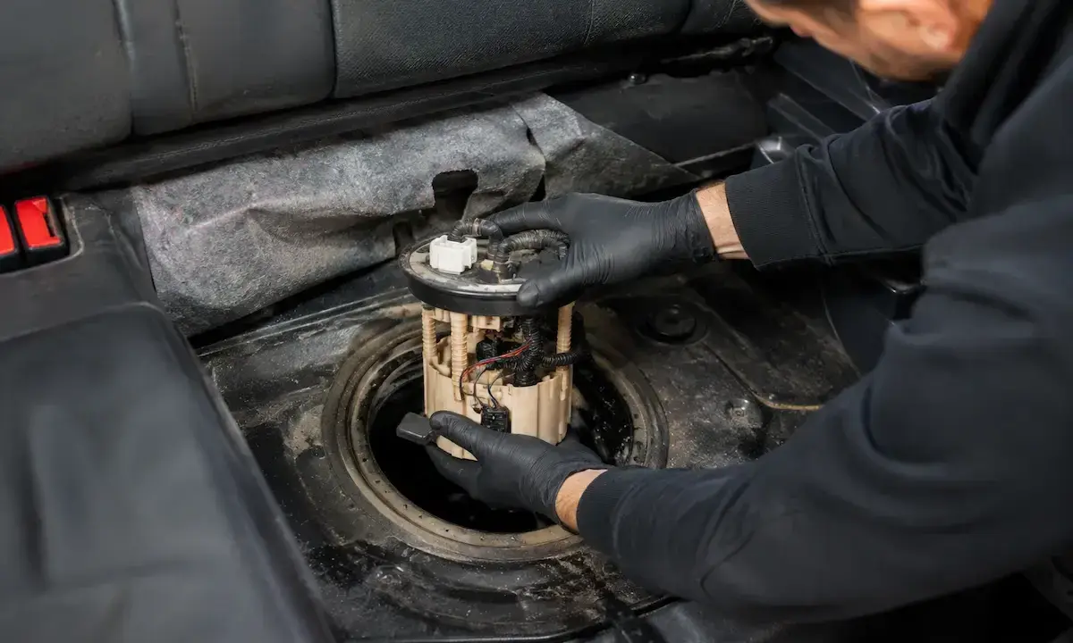Mechanik w czarnych rękawiczkach wyjmuje moduł pompy paliwa z baku samochodu. To może być objaw uszkodzonej pompy paliwa.