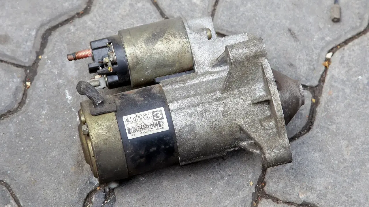 Dwa używane rozruszniki samochodowe, gotowe do wymiany. Jeden z nich ma naklejkę z numerem MC0JT82081.