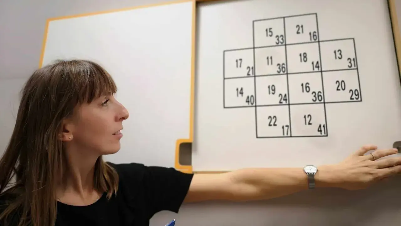 Psycholog ocenia zdolności poznawcze podczas testu psychologicznego dla kierowców. Na tablicy widoczny jest schemat z liczbami.