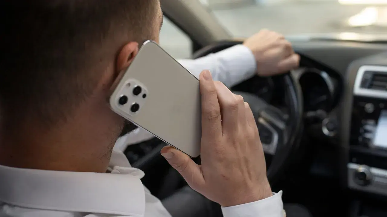 Mężczyzna rozmawia przez telefon, trzymając kierownicę. Ryzykowne korzystanie z telefonu podczas jazdy.
