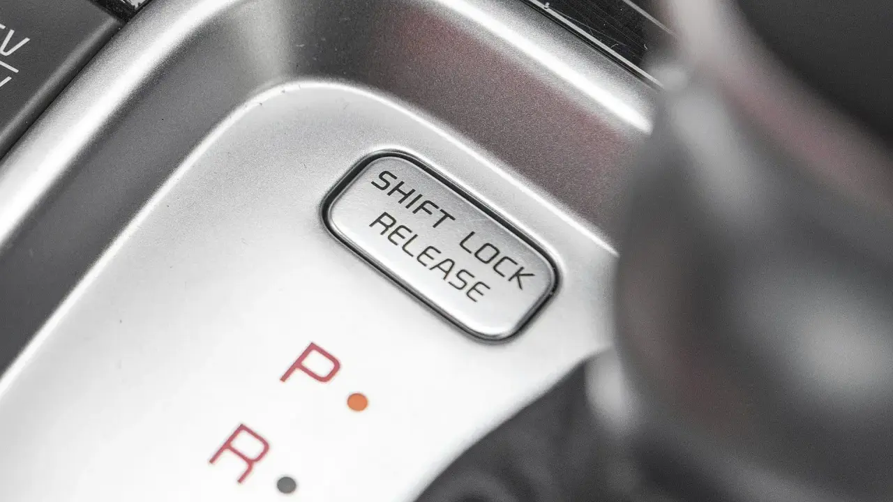 Przycisk "SHIFT LOCK RELEASE" na konsoli środkowej, obok oznaczeń biegów P i R.