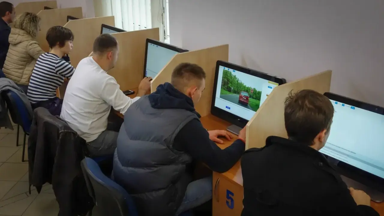 Ludzie siedzą przy komputerach, rozwiązując testy. To miejsce, gdzie można sprawdzić, kiedy można zdawać egzamin teoretyczny na prawo jazdy.