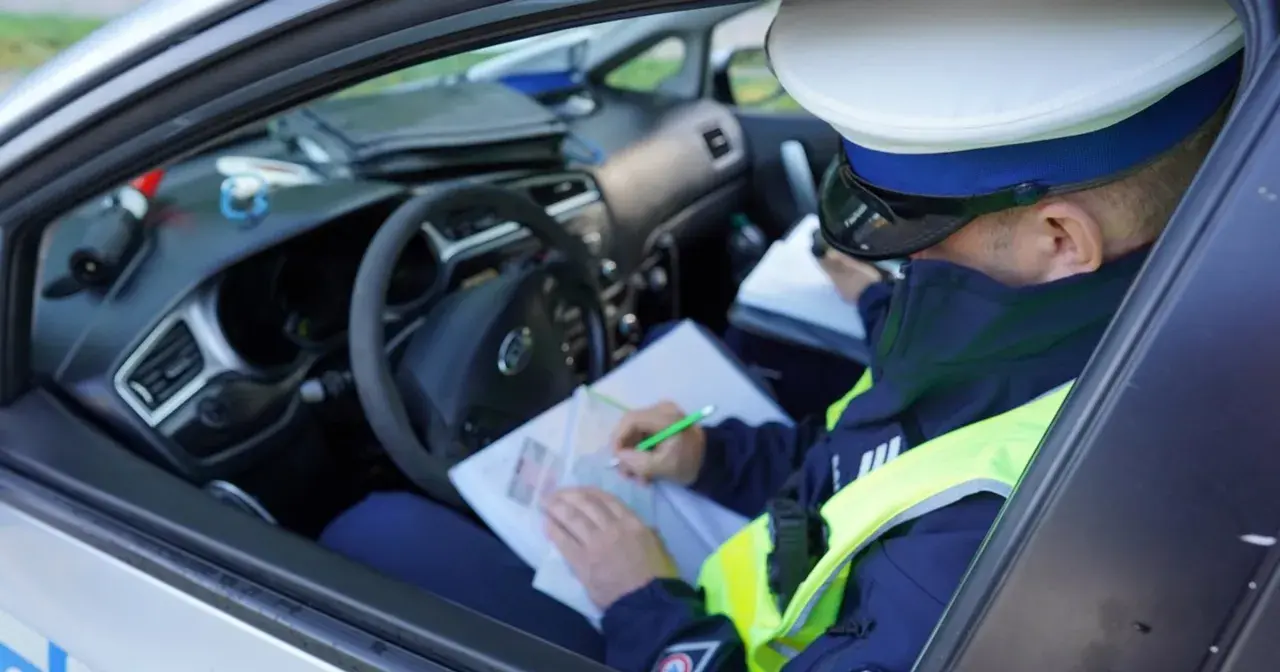 Policjant w radiowozie wypisuje mandat za jazdę bez kasku.
