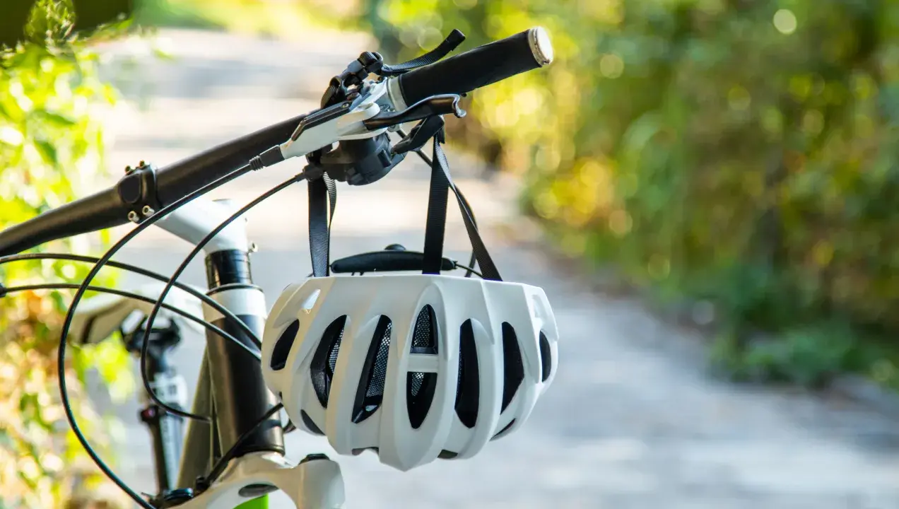 Biały kask rowerowy wisi na kierownicy roweru. Pamiętaj o kasku, by uniknąć mandatu za brak kasku na rowerze.