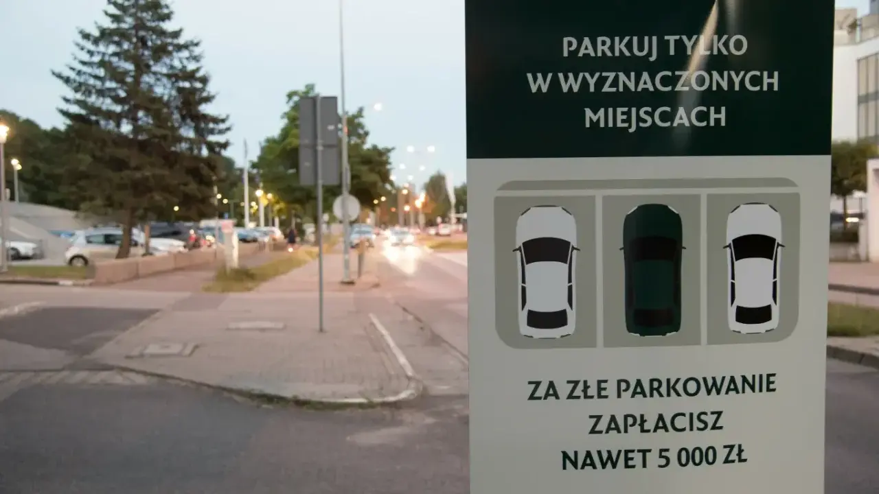 Znak informuje: "Parkuj tylko w wyznaczonych miejscach. Za złe parkowanie zapłacisz nawet 5000 zł". Straż miejska pilnuje porządku.