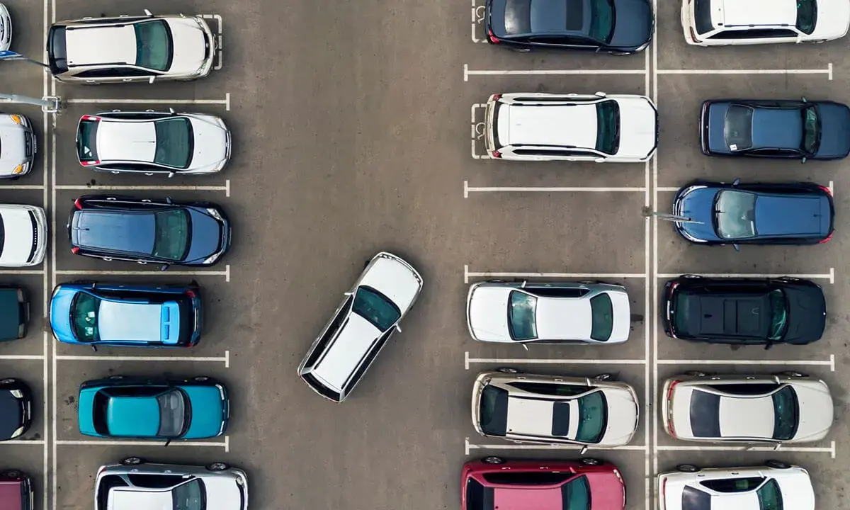 Widok z góry na parking. Po prawej stronie zaparkowane są samochody w rzędzie, jeden za drugim.