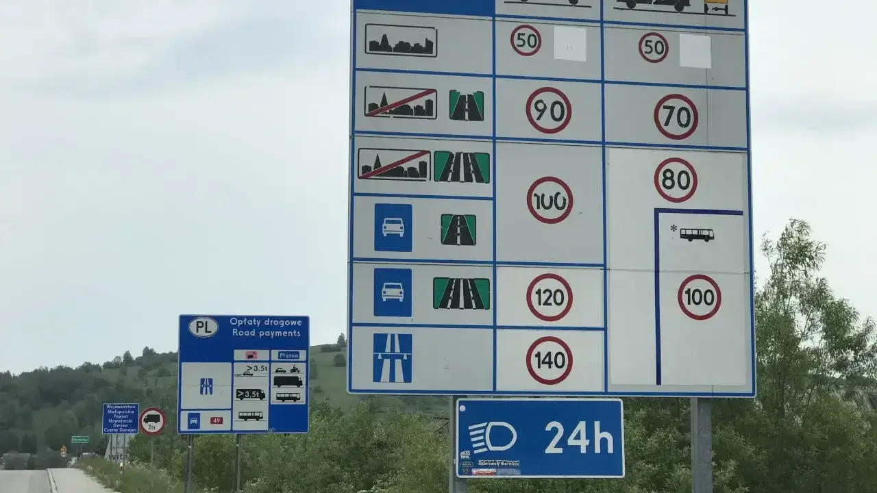 Znaki drogowe informujące o opłatach i limitach prędkości na drodze jednojezdniowej dwukierunkowej.