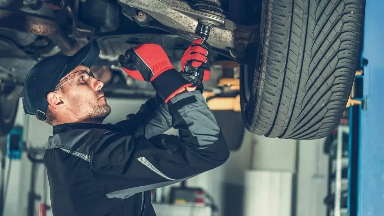 Mechanik dokręca sworzeń w zawieszeniu auta, pracując pod podniesionym pojazdem.