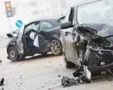 Dwa zniszczone samochody na drodze. W jednym z nich widać siedzącego człowieka po wypadku samochodowym, z otwartymi drzwiami i poduszką powietrzną.