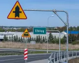 Uwaga na skrzyżowanie z drogą podporządkowaną i przejazd kolejowy. Znak "Elbląg" zaprasza do miasta.