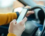 Ręka trzymająca telefon za kierownicą. Zastanawiasz się, ile punktów za telefon stracisz?