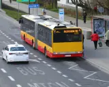 Żółto-czerwony autobus przegubowy linii 182 zbliża się do przystanku. Czy autobus ma pierwszeństwo przed białym autem taxi?