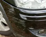 Zarysowany zderzak czarnego samochodu. Widać liczne rysy, które mogą być podstawą do roszczeń z OC sprawcy.