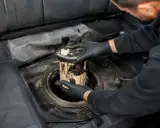 Mechanik w czarnych rękawiczkach wyjmuje moduł pompy paliwa z baku samochodu. To może być objaw uszkodzonej pompy paliwa.