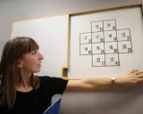 Psycholog ocenia zdolności poznawcze podczas testu psychologicznego dla kierowców. Na tablicy widoczny jest schemat z liczbami.