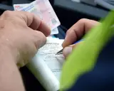 Ręce wypełniają formularz mandatu karnego, próbując dokonać przepisanie mandatu na inną osobę. Widoczne prawo jazdy.