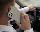 Mężczyzna rozmawia przez telefon, trzymając kierownicę. Ryzykowne korzystanie z telefonu podczas jazdy.