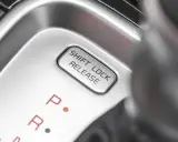Przycisk "SHIFT LOCK RELEASE" na konsoli środkowej, obok oznaczeń biegów P i R.