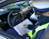 Policjant w radiowozie wypisuje mandat za jazdę bez kasku.