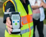 Policjant trzyma alkomat, który pokazuje wynik 0.93. To urządzenie pomaga sprawdzić, co neutralizuje alkohol w wydychanym powietrzu.