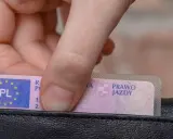 Dłoń wkłada do portfela polskie prawo jazdy. Czy trzeba mieć przy sobie dokument?