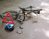 Potrącenie rowerzysty na ścieżce rowerowej. Leżący rower, kask, okulary i trójkąt ostrzegawczy sugerują wypadek.