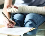 Osoba z ręką w gipsie wypełnia dokumenty. Wzór pzu opis zdarzenia jest gotowy do wypełnienia.