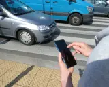 Osoba z telefonem na przejściu dla pieszych, kiedy należy zachować szczególną ostrożność. Samochody i niebieski van na drodze.