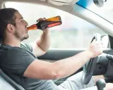 Mężczyzna pije piwo za kierownicą. Powyżej 0,5 promila jaka kara grozi za jazdę pod wpływem alkoholu.