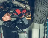 Mechanik dokręca sworzeń w zawieszeniu auta, pracując pod podniesionym pojazdem.