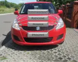 Czerwony Suzuki Swift z etykietami: kierunkowskazy, pozycyjne, mijania, drogowe. Idealny do nauki przed egzaminem na prawo jazdy.