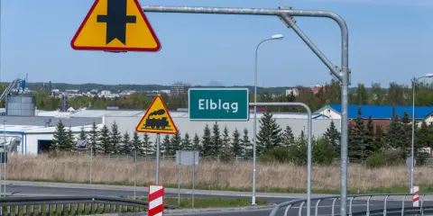 Uwaga na skrzyżowanie z drogą podporządkowaną i przejazd kolejowy. Znak "Elbląg" zaprasza do miasta.