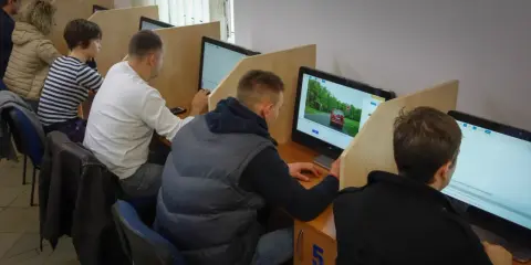 Ludzie siedzą przy komputerach, rozwiązując testy. To miejsce, gdzie można sprawdzić, kiedy można zdawać egzamin teoretyczny na prawo jazdy.