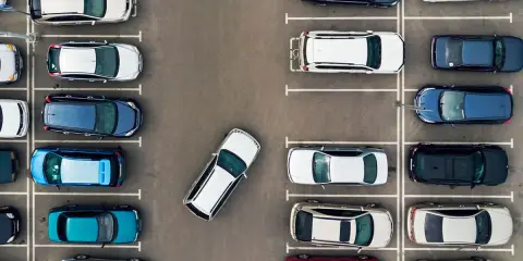 Widok z góry na parking. Po prawej stronie zaparkowane są samochody w rzędzie, jeden za drugim.