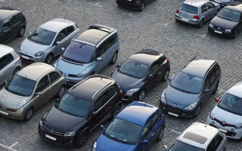 Na parkingu stoi wiele samochodów. Jeden z nich, srebrny Nissan, wygląda na uszkodzony. Czy to szkoda parkingowa? Policja już tu jest.