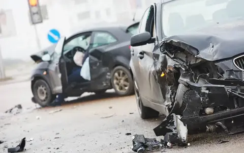 Dwa zniszczone samochody na drodze. W jednym z nich widać siedzącego człowieka po wypadku samochodowym, z otwartymi drzwiami i poduszką powietrzną.