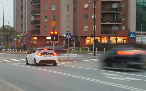 Biały samochód czeka na zielone światło. Czerwone światło oznacza punkty karne.