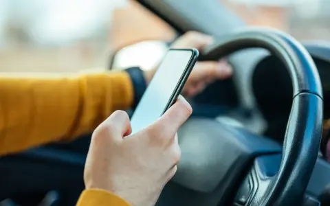 Ręka trzymająca telefon za kierownicą. Zastanawiasz się, ile punktów za telefon stracisz?