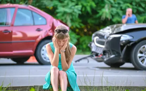 Kobieta w szoku po spowodowaniu wypadku z uszczerbkiem na zdrowiu powyżej 7 dni. Dwa uszkodzone samochody na drodze.