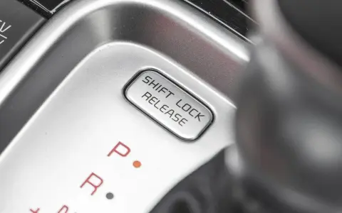 Przycisk "SHIFT LOCK RELEASE" na konsoli środkowej, obok oznaczeń biegów P i R.
