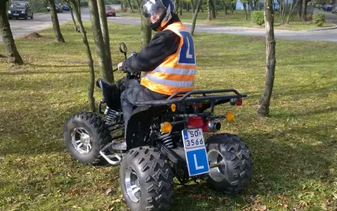 Chcesz wiedzieć, jakie prawo jazdy na quada? Kierowca w kamizelce odblaskowej i kasku siedzi na quadzie, gotowy do jazdy.