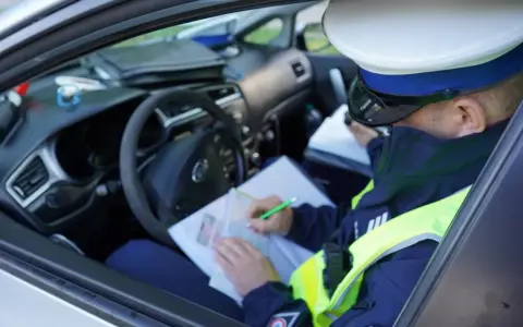Policjant w radiowozie wypisuje mandat za jazdę bez kasku.