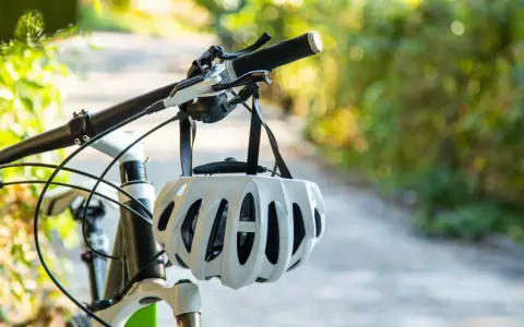 Biały kask rowerowy wisi na kierownicy roweru. Pamiętaj o kasku, by uniknąć mandatu za brak kasku na rowerze.