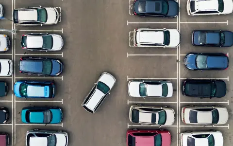 Widok z góry na parking. Po prawej stronie zaparkowane są samochody w rzędzie, jeden za drugim.