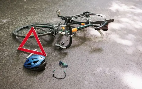 Potrącenie rowerzysty na ścieżce rowerowej. Leżący rower, kask, okulary i trójkąt ostrzegawczy sugerują wypadek.
