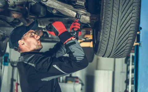 Mechanik dokręca sworzeń w zawieszeniu auta, pracując pod podniesionym pojazdem.